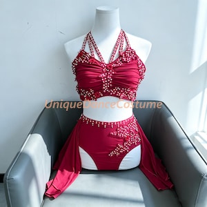 May include: A two-piece dark red dance costume featuring a halter-style crop top with multiple straps and high-waisted bottoms. The set is adorned with white pearl-like beads and small fabric roses. The text UniqueDanceCostume is visible.
