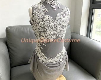 May include: A sleeveless grey leotard featuring a high neckline and intricate white lace appliqué adorned with clear crystals and small white beads. The garment includes a layered chiffon skirt overlay and the text UniqueDanceCostume.