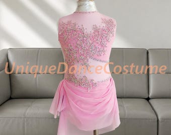 May include: A sleeveless light pink dance costume featuring a sheer bodice adorned with intricate silver floral embroidery and sparkling crystals. The skirt consists of layered, flowing pink chiffon fabric. The text UniqueDanceCostume is visible.