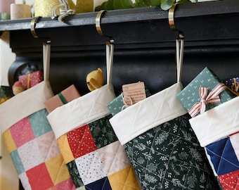 Puede incluir: Cuatro calcetines de Navidad colgando de una repisa de chimenea negra. Los calcetines están hechos de diferentes telas y patrones, incluyendo un diseño de patchwork, un diseño floral verde y un diseño de lunares verde y blanco. Los calcetines están llenos de pequeños regalos y una nota que dice "Colgaron sus calcetines y luego se fueron a la cama, con la esperanza de regalos para la noche siguiente."