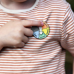 Little boy spinning an arrow on a spinning pin badge reading today i am enough in the green segment of the six segment multicolour pin badge.