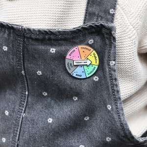 child wearing today i am spinner pin badge on grey denim dungarees. Spinner arrow is pointing at 'Today I am hopeful'