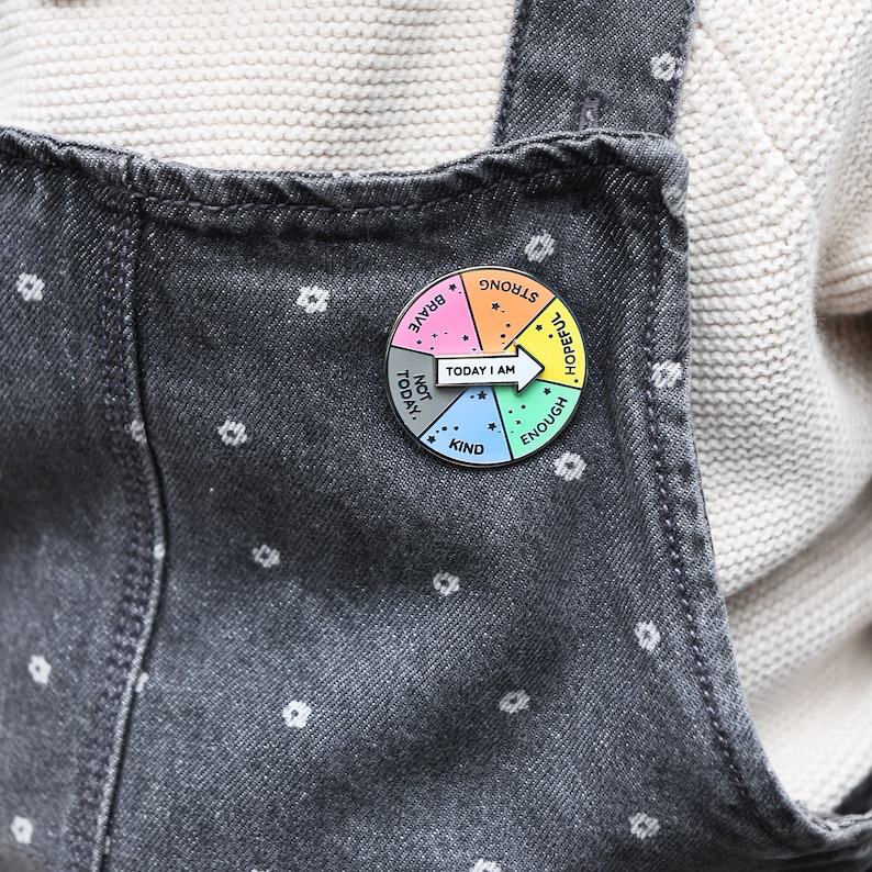 child wearing today i am spinner pin badge on grey denim dungarees. Spinner arrow is pointing at 'Today I am hopeful'