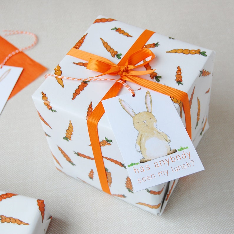 May include: A white gift box with an orange ribbon and a carrot pattern. The gift tag has a cartoon bunny and the text "has anybody seen my lunch?"