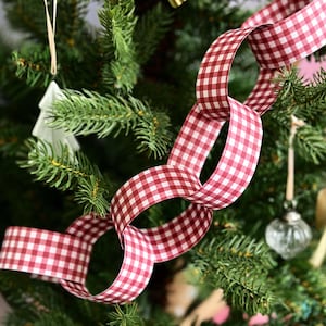 May include: A Christmas tree adorned with a red and white gingham ribbon garland. The garland is looped and intertwined, creating a festive and decorative element. Other ornaments are visible.