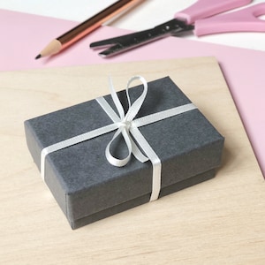 Deep grey luxurious gift box for pin badge with eco-friendly ivory skinny ribbon tied in a bow around the box.