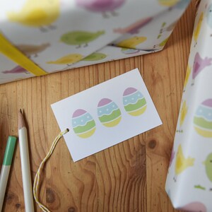 May include: A white gift tag with three pastel Easter eggs on it. The eggs are decorated with green, blue, and yellow stripes and white dots.