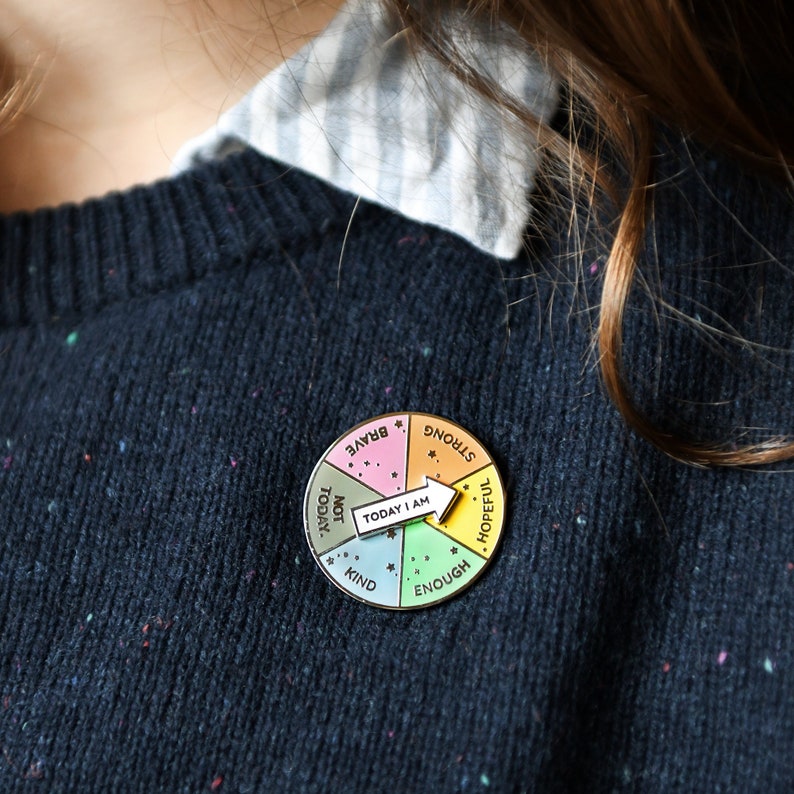 Rainbow Enamel pin badge with a white spinner to select your mood of the day. Badge is attached to a navy blue knitted jumper with 'today i am' spinner pointing at the word hopeful.