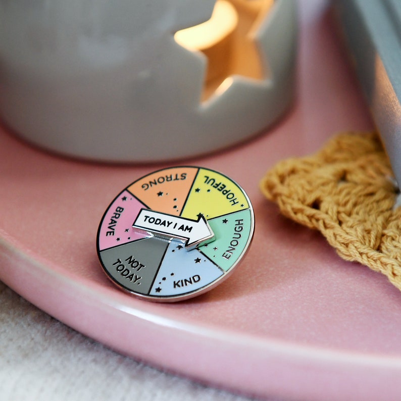 Today I am enough multiple options pin badge with spinning arrow. Each segment on the badge has a different colour and different words. Orange is strongwomen, yellow is hopeful, green is enough, blue is kind, grey is not today and pink is brave.
