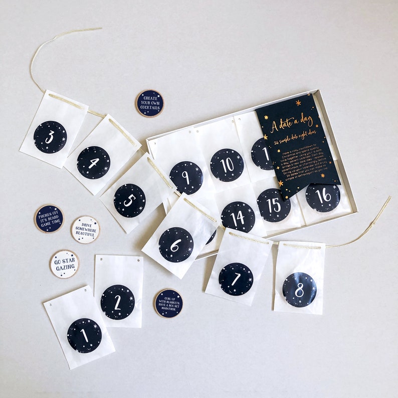 A couples date night ideas advent calendar with several wooden tokens, each with a date activity on, and a string of numbered envelopes lays on a grey surface.