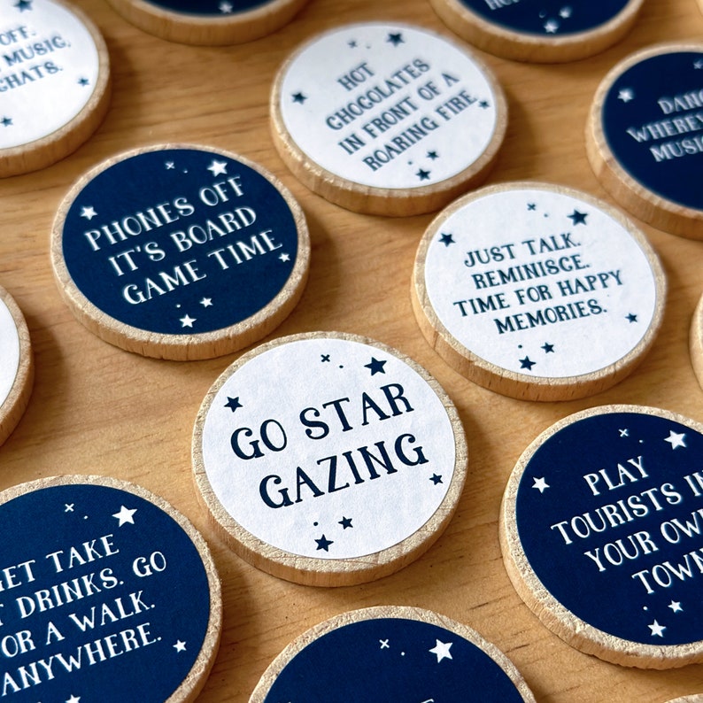 Twenty four wooden tokens, each with a recycled label that have a date night idea printed on, lay on a wooden desk.