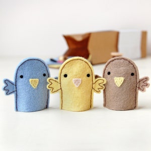 May include: Three felt finger puppets shaped like birds. The bird on the left is blue, the middle bird is yellow, and the bird on the right is brown.