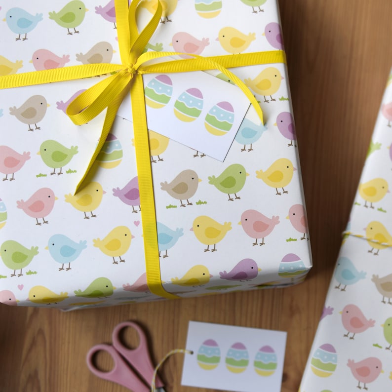 May include: A white gift wrap with a yellow ribbon and a tag. The gift wrap has a pattern of colorful birds and eggs. The tag has a pattern of three colorful eggs.
