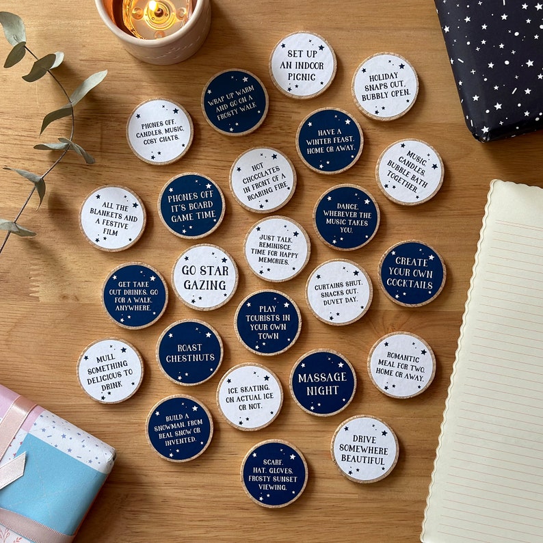 Twenty four wooden tokens, each with a recycled label that have a date night idea printed on, lay on a wooden desk.