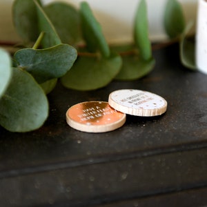 2 wooden disks with copper foiled stickers stuck on the top of them are placed on top of a black mantle piece surrounded by green leaves.