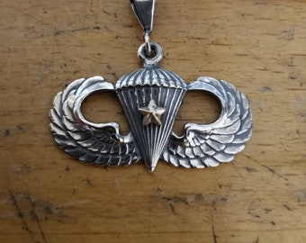 May include: Silver pendant with a parachute and wings design. The parachute has a gold star in the center.