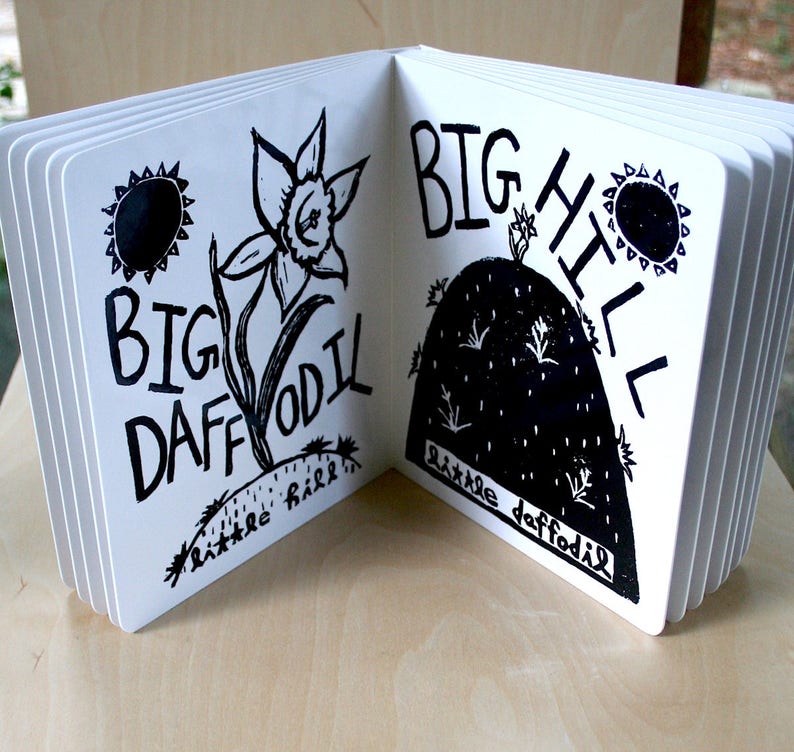 K&ouml;nnte beinhalten: Ein schwarz-wei&szlig; illustriertes Kinderbuch mit dem Text "Big Daffodil" auf der linken Seite und "Big Hill" auf der rechten Seite. Die linke Seite zeigt eine gro&szlig;e Narzisse mit einer Sonne dar&uuml;ber. Die rechte Seite zeigt einen gro&szlig;en H&uuml;gel mit einer kleinen Narzisse oben.