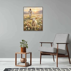 K&ouml;nnte beinhalten: Ein gerahmtes Gem&auml;lde zeigt ein Lamm in einem Blumenfeld, mit einer Figur im Hintergrund. Das Kunstwerk wird an einer grauen Wand neben einem h&ouml;lzernen Beistelltisch mit einer Pflanze und einem gemusterten Stuhl ausgestellt.