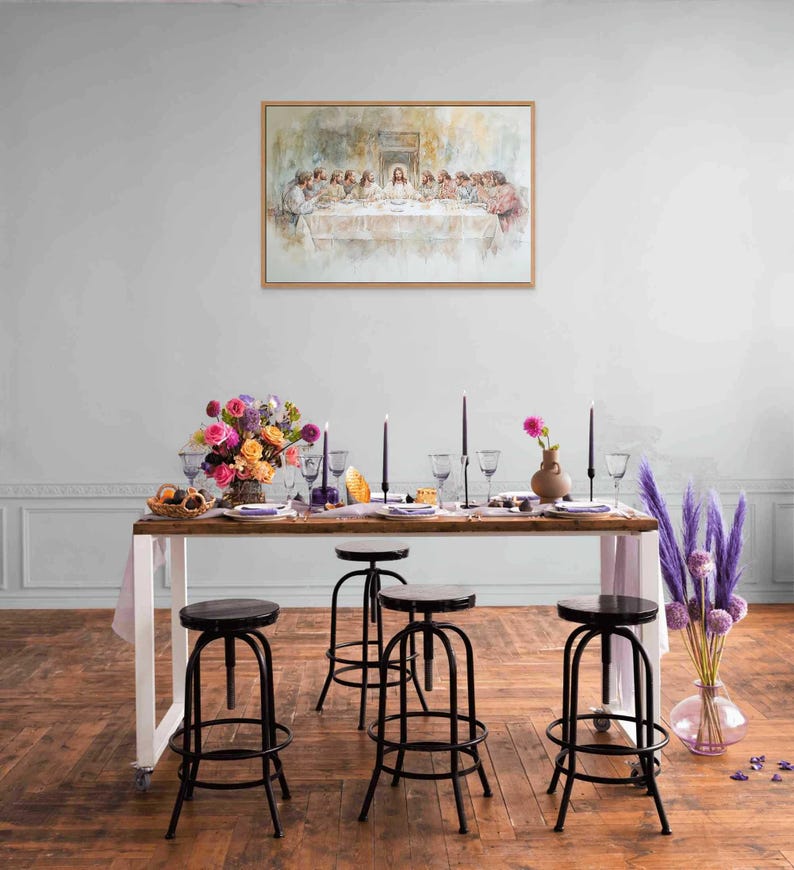 May include: A white table with a wooden top is set with a floral centerpiece, candles, and glasses.  Black metal stools surround the table. A framed painting of the Last Supper hangs on the wall behind the table.