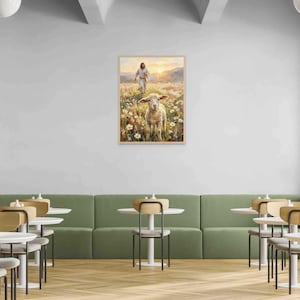 K&ouml;nnte beinhalten: Ein gerahmtes Gem&auml;lde zeigt eine Figur, die auf ein Schaf in einem Feld mit Wildblumen zugeht. Das Kunstwerk wird an einer wei&szlig;en Wand &uuml;ber einer gr&uuml;nen Bank mit kleinen runden Tischen und St&uuml;hlen in einem Caf&eacute;-Ambiente ausgestellt.