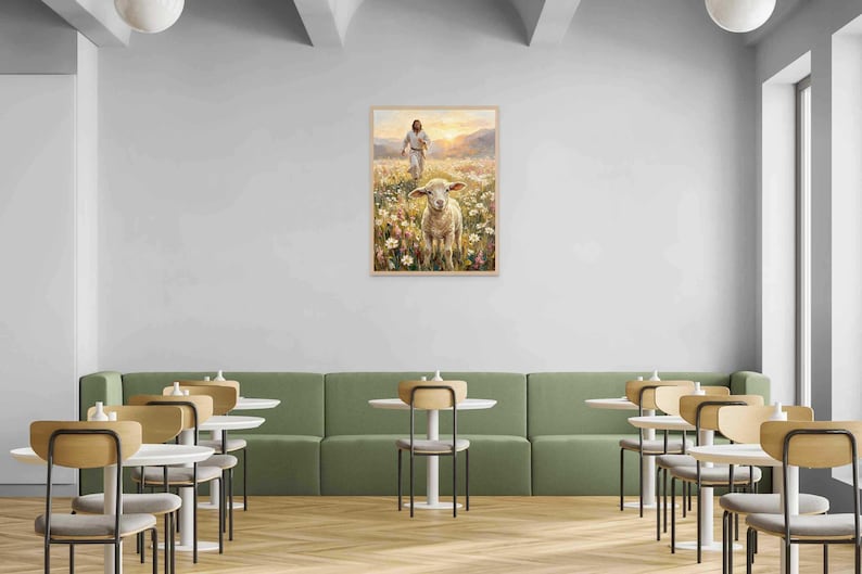 K&ouml;nnte beinhalten: Ein gerahmtes Gem&auml;lde zeigt eine Figur, die auf ein Schaf in einem Feld mit Wildblumen zugeht. Das Kunstwerk wird an einer wei&szlig;en Wand &uuml;ber einer gr&uuml;nen Bank mit kleinen runden Tischen und St&uuml;hlen in einem Caf&eacute;-Ambiente ausgestellt.