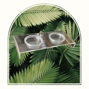 Puede incluir: Un comedero para mascotas de acrílico transparente con dos cuencos de plástico transparente. El comedero está diseñado para ser montado en una pared o jaula.