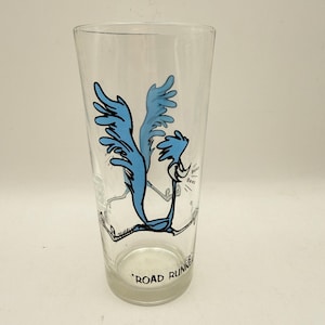 May include: A clear glass tumbler featuring a blue Road Runner cartoon character in a running pose. The graphic includes the text Beep Beep near the character and the words ROAD RUNNER printed in black near the base of the glass.