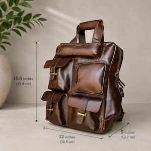 May include: A brown leather backpack with multiple pockets and compartments. The bag has a top handle and adjustable straps. It measures 15.5 inches (39.4 cm) high, 12 inches (30.5 cm) wide, and 5 inches (12.7 cm) deep. Gold-colored hardware accents the bag.