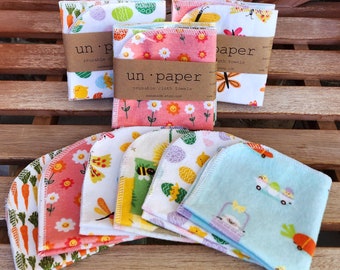 Könnte beinhalten: Wiederverwendbare Stoffhandtücher mit Frühlingsmotiven. Designs umfassen Karotten, Blumen, Schmetterlinge, Bienen, Ostereier und Küken. Die Handtücher sind mit braunen Papierbändern gebündelt, die "un paper reusable cloth towels" lesen.