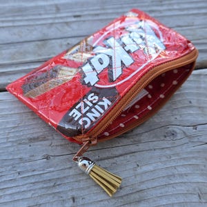 May include: A red and brown zippered pouch made from a Kit Kat candy wrapper. The pouch features the Kit Kat logo and the words "KING SIZE". The interior lining is red with white polka dots, and the zipper pull has a gold tassel.
