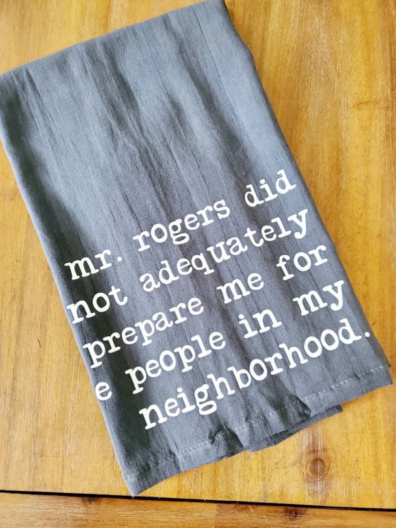 Pu&ograve; includere: Un asciugamano da cucina grigio con testo bianco che recita "mr. rogers did not adequately prepare me for the people in my neighborhood."
