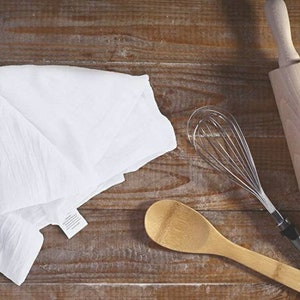 Pu&ograve; includere: Un asciugamano da cucina bianco, un cucchiaio di legno, una frusta di filo metallico e un mattarello di legno su una superficie di legno.