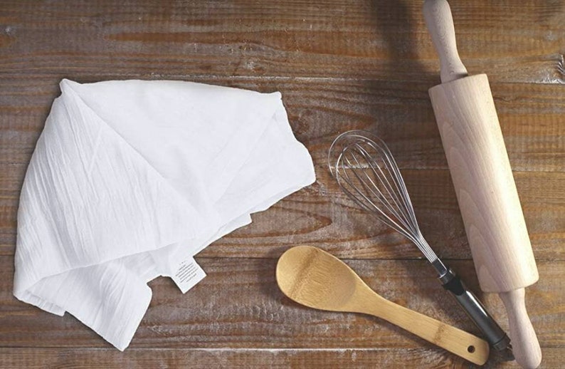 Pu&ograve; includere: Un asciugamano da cucina bianco, un cucchiaio di legno, una frusta di filo metallico e un mattarello di legno su una superficie di legno.