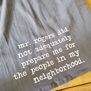 Pu&ograve; includere: Un asciugamano da cucina grigio con testo bianco che dice "mr. rogers did not adequately prepare me for the people in my neighborhood."