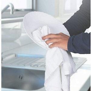 Pu&ograve; includere: Un piatto in ceramica bianca viene asciugato con un canovaccio bianco in un lavandino da cucina.
