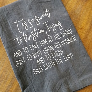 May include: Gray kitchen towel with white text that reads "Tis so sweet to trust in Jesus and to take Him at His word just to rest upon His promise and to know thus saith the Lord."