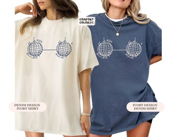 May include: Two t-shirts, one ivory and one denim blue, each featuring a graphic of two disco balls connected by a line. The text "Olivia's Bach" and "Nashville" are below the disco balls. The ivory shirt has "Denim Design Ivory Shirt" text.