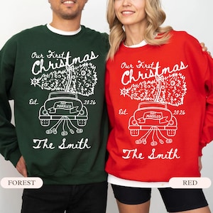 Pu&ograve; includere: Una felpa verde bosco e una felpa rossa, entrambe con una grafica bianca di un'auto che trasporta un albero di Natale con il testo Our First Christmas, Est. 2026, Just Married e The Smith stampato in un carattere corsivo bianco.