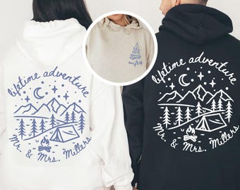 May include: White and black hoodies with matching camping-themed designs. The white hoodie features a blue mountain and tent graphic with the text "lifetime adventure" and "Mr. & Mrs. Millers." The black hoodie has a similar design in white.