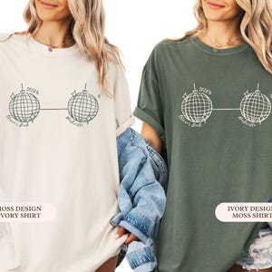 May include: Two oversized t-shirts, one cream and one dark green, each with a graphic of two disco balls linked by a line. The text "2025" is above the disco balls, with "Olivia's Bach" and "Nashville" below. The cream shirt is labelled "Moss Design Ivory Shirt".