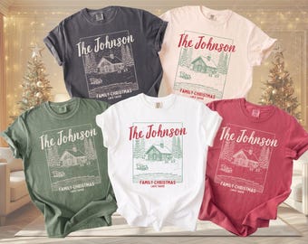 May include: Five short-sleeve crew neck t-shirts in charcoal, light pink, olive green, white, and red. Each shirt features a graphic of a cabin in the woods with the text The Johnson, FAMILY-CHRISTMAS, and LAKE TAHOE printed in a rectangular frame.