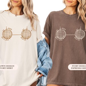 May include: Two t-shirts, one ivory and one espresso, each with a brown graphic of two disco balls linked by a line. The text "Olivia's Bach" and "Nashville" are printed below. The ivory shirt has a brown design, and the espresso shirt has an ivory design.