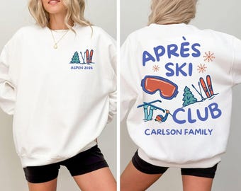 May include: White sweatshirt with a ski-themed design. The front features a small graphic with a tree, skis, and the text "ASPEN 2026." The back displays "APRÈS SKI CLUB" with ski goggles, skis, a tree, and "CARLSON FAMILY."