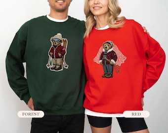 May include: Forest green and red sweatshirts with embroidered bear designs. The bears are dressed in winter ski attire, complete with goggles, skis, and jackets. The sweatshirts have a crew neck and long sleeves.