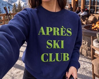 May include: A navy blue crewneck sweatshirt featuring the text APRÈS SKI CLUB in raised, lime green lettering across the chest. The garment has long sleeves and a ribbed neckline, providing a simple and functional design for casual wear.