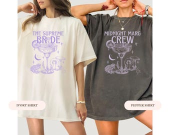 May include: Two oversized t-shirts, one ivory and one pepper, featuring a margarita glass design with the text "THE SUPREME BRIDE" and "MIDNIGHT MARG CREW" in lavender. The design includes a moon, mushrooms, and a frog.