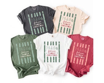 May include: Five short-sleeve crew neck t-shirts in charcoal, cream, olive green, white, and red. Each shirt features a central graphic with vertical stripes, holiday icons like a candy cane and gingerbread man, and the text Johnson FAMILY CHRISTMAS.