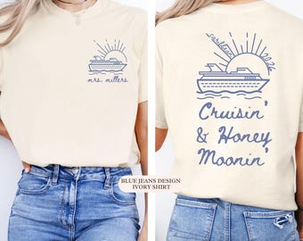 May include: Ivory t-shirt with a blue cruise ship and sun graphic. The front says "mrs. millers" and the back says "Cruisin' & Honey Moonin'" with "Caribbean 2026". The shirt is paired with blue jeans.