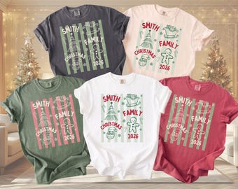 May include: Five short-sleeve crew neck t-shirts in charcoal, cream, olive green, white, and red. Each shirt features a graphic with vertical stripes, a Christmas tree, a sleigh, a gingerbread man, Santa, and the text Smith Family Christmas 2026.