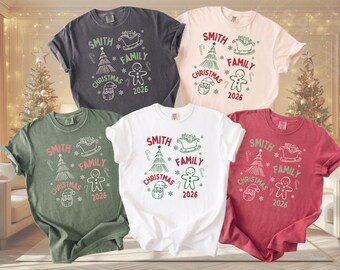 May include: Five short-sleeved t-shirts in charcoal, cream, olive green, white, and red. Each shirt features a graphic print with the text Smith Family Christmas 2026, accompanied by illustrations of a sleigh, a Christmas tree, a gingerbread person, and Santa.